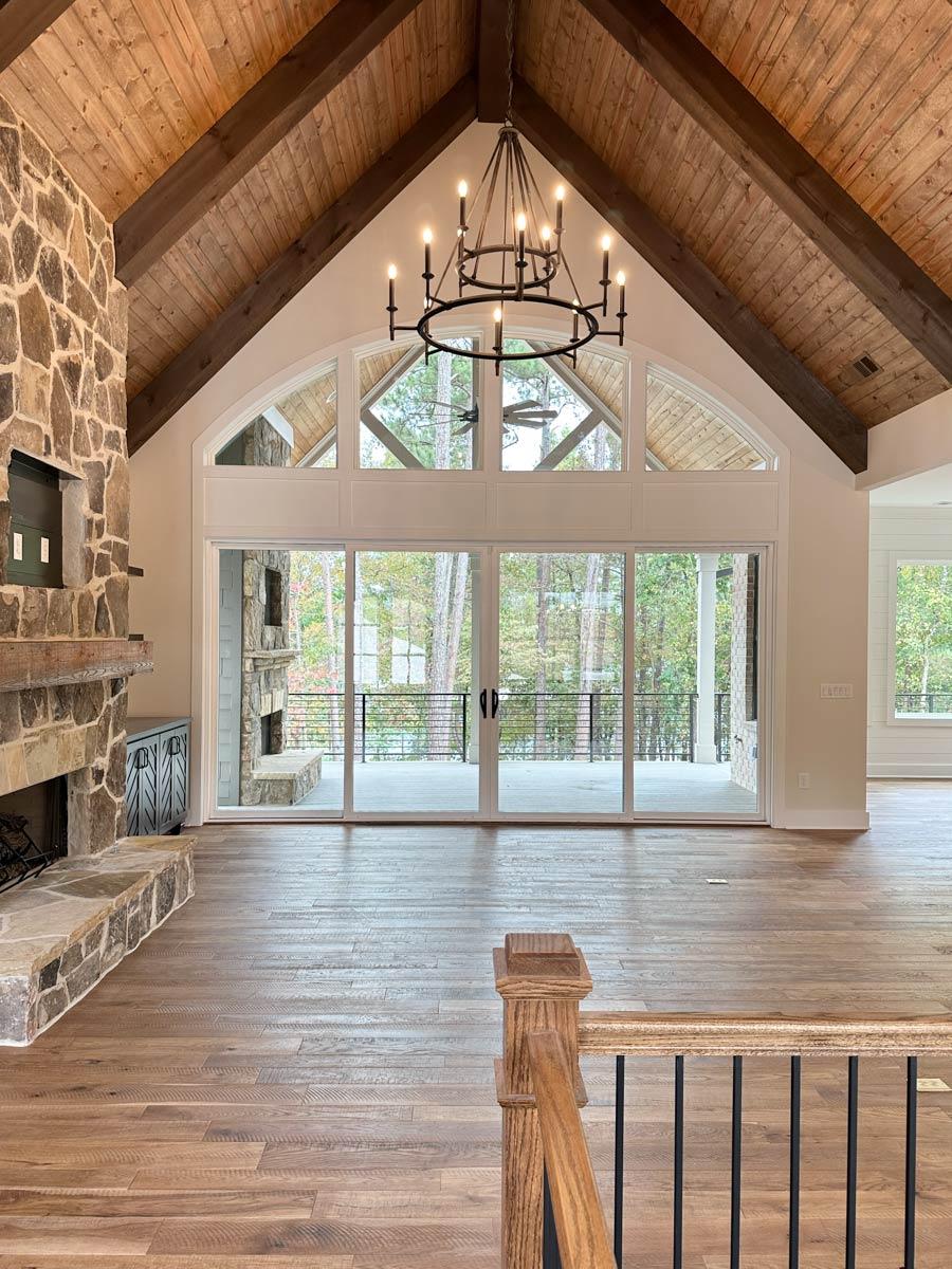 Vaulted wood-beamed ceiling with a large arched window and fireplace in a great room with wood floors.