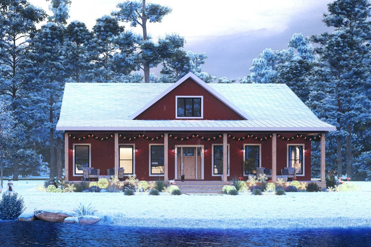 A festive red house covered in snow, with a snowy roof, is decorated with lights. Snowy trees surround the house, beside a body of water.
