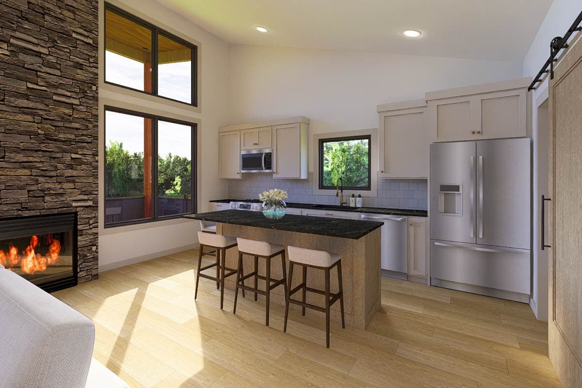Interior view of open-concept kitchen and great room with stone fireplace, island with bar stools, vaulted ceiling, and large windows.