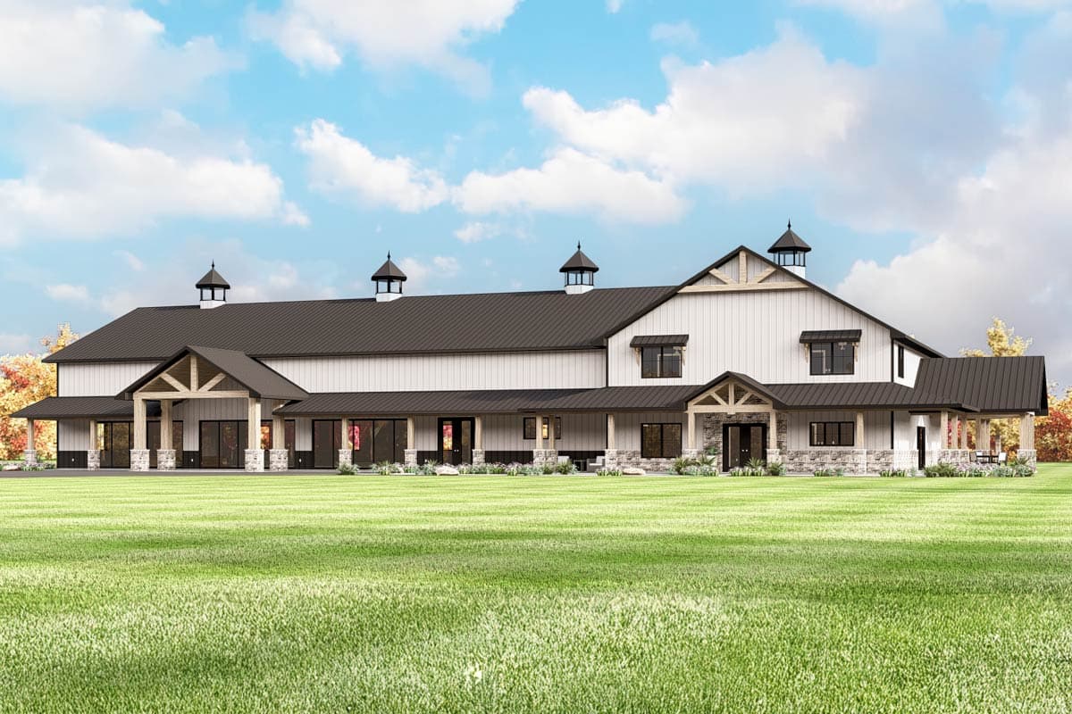 House plan exterior: Large white barn-style building with dark metal roof, gabled dormers, covered porches, and stone accents.