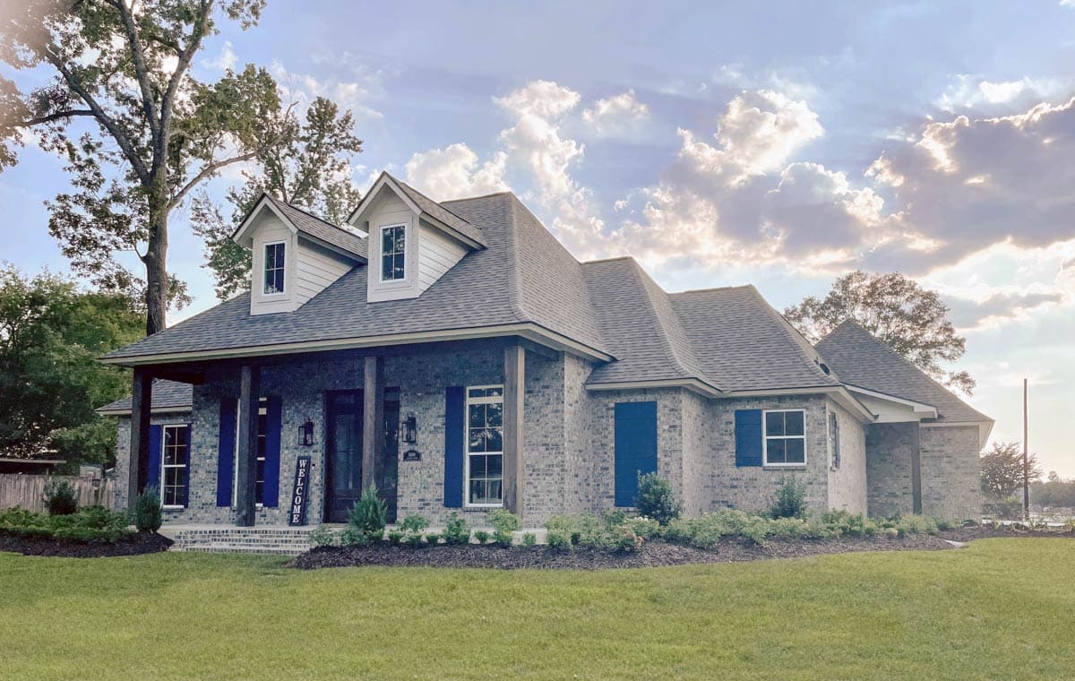 House plan exterior: two-story brick home with a covered front porch, dormer windows, and dark blue shutters.