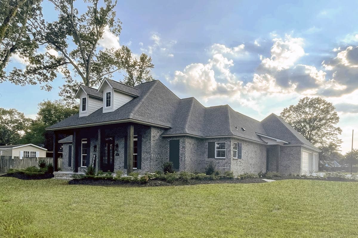 House plan exterior featuring a brick facade, prominent gabled dormers, a covered porch with dark columns, and a two-car garage.