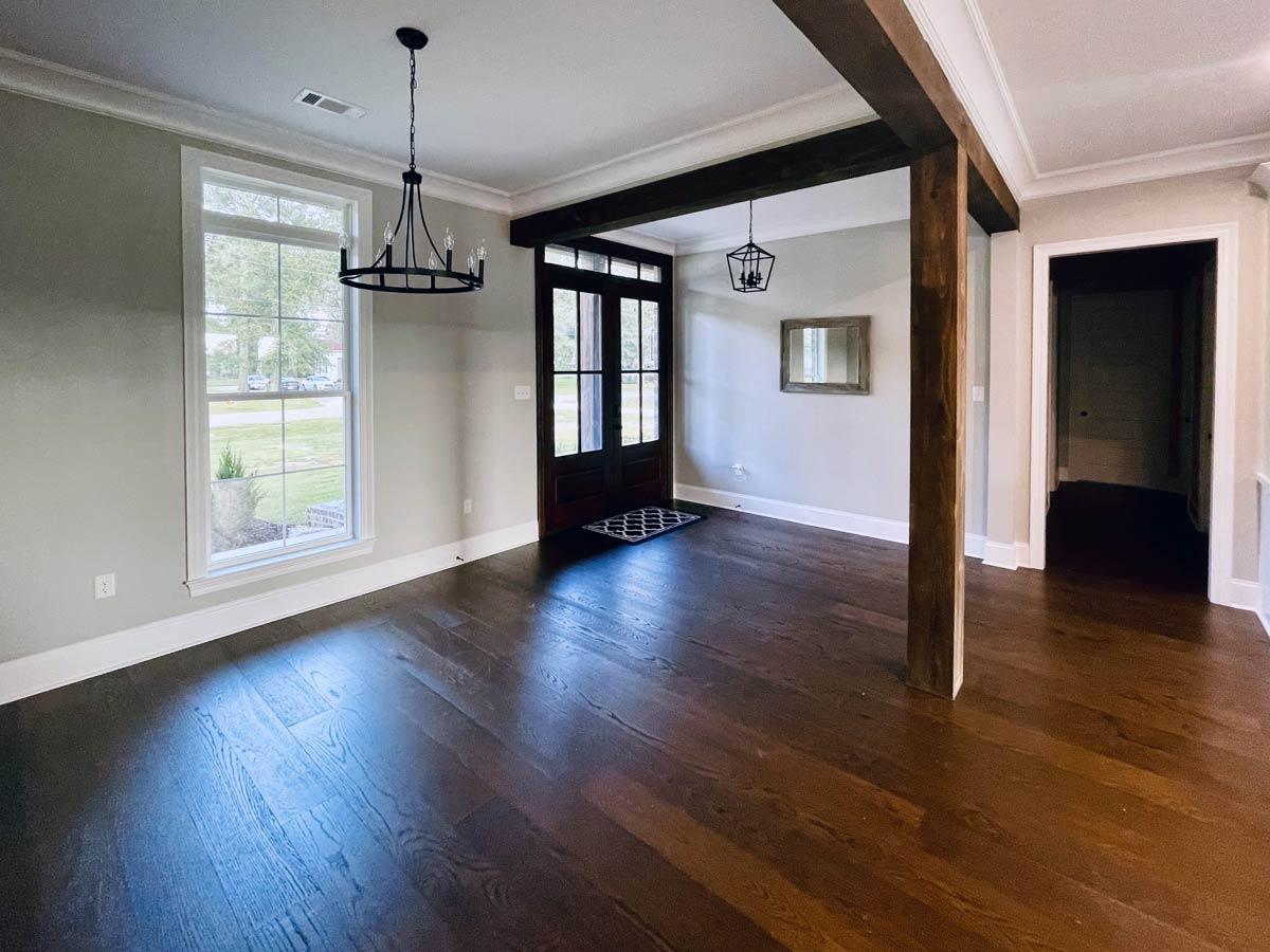 Interior view of a house plan showing an entryway with dark wood flooring, a wooden beam accent, and a large window.