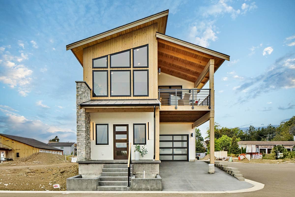 House plan exterior. Modern two-story house with a balcony, glass garage door, a shed roof, and stone accents.