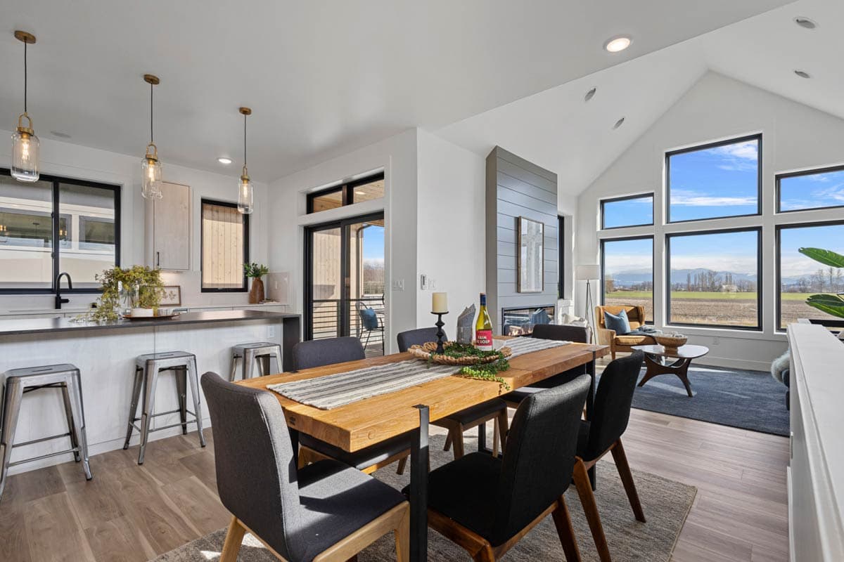 Open concept living area with kitchen island, dining table, fireplace, and vaulted ceiling with large windows.