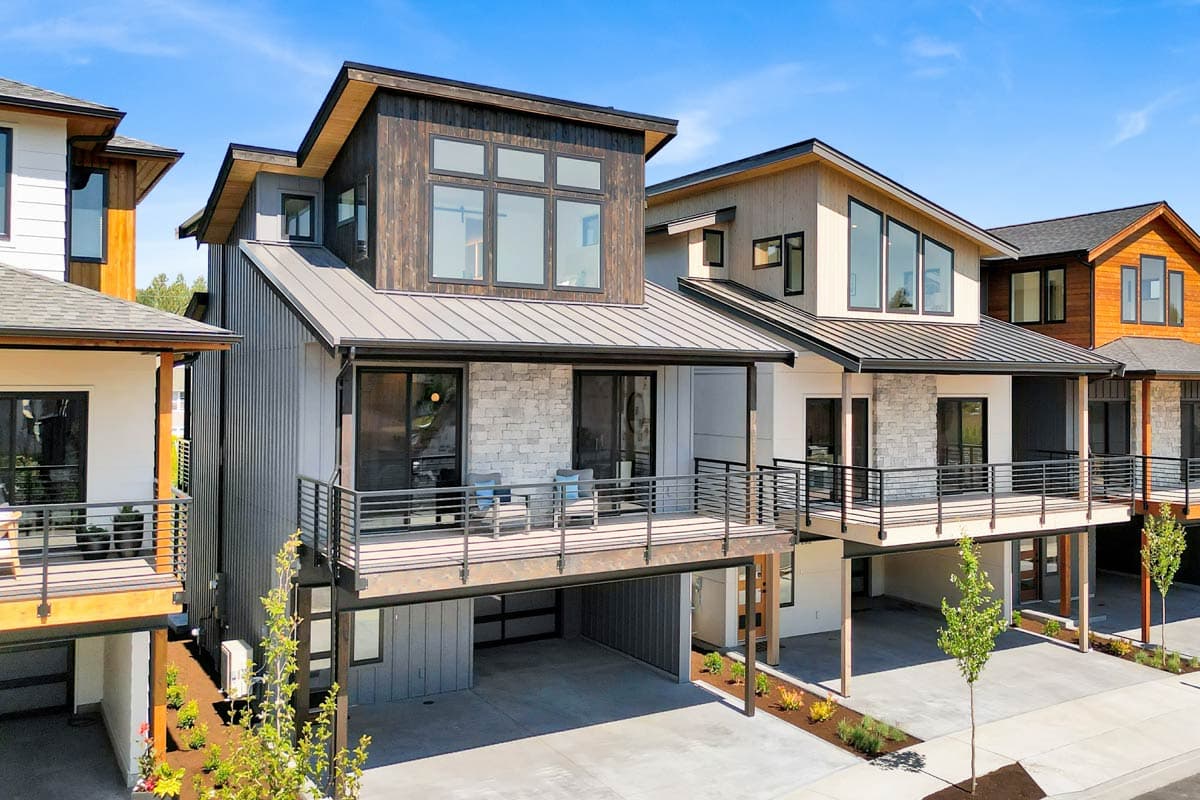 Modern house plan exterior with metal roof, stone and wood siding, elevated deck, and open garage.