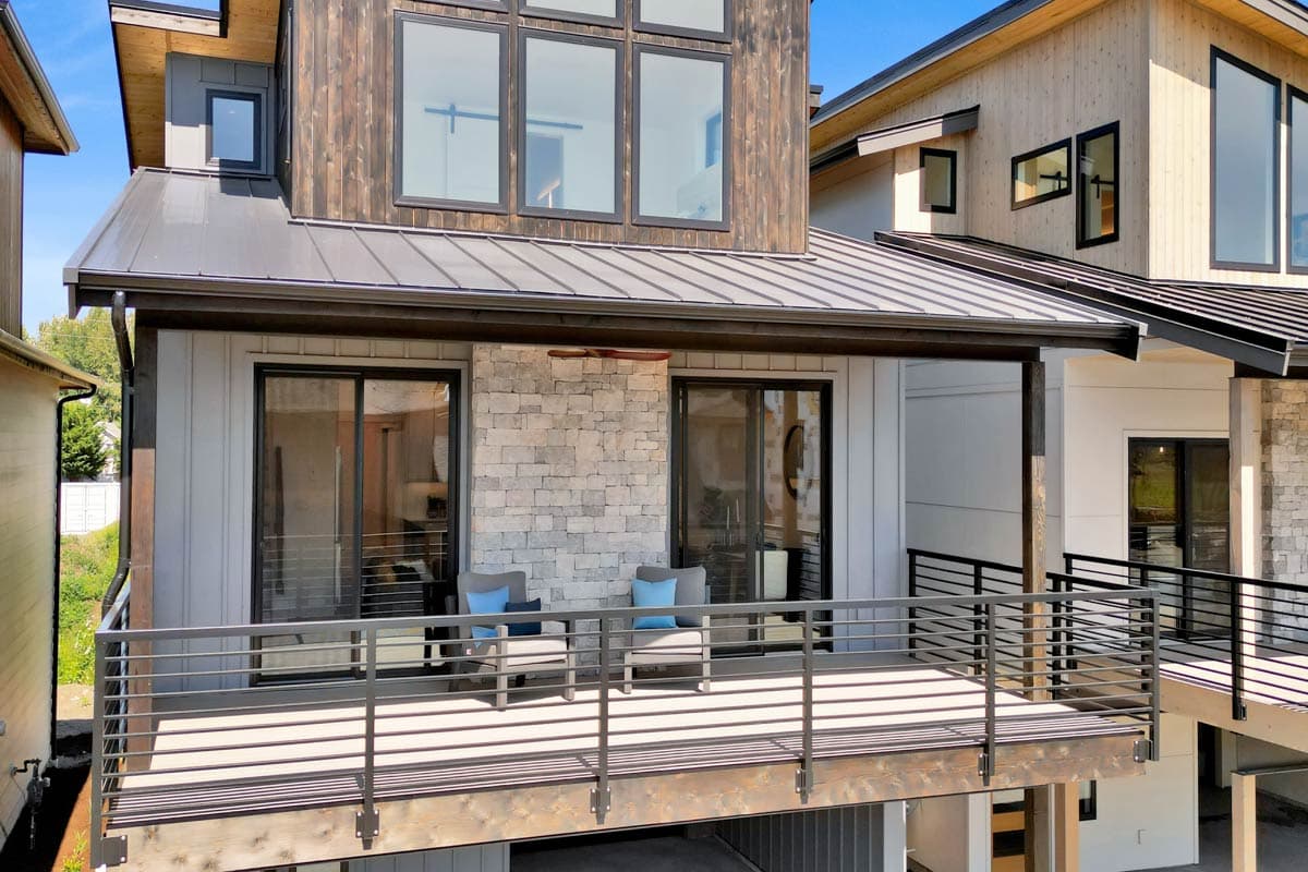 House plan exterior: Modern style, two stories, metal roof, stone and wood siding, multiple large windows, and deck.