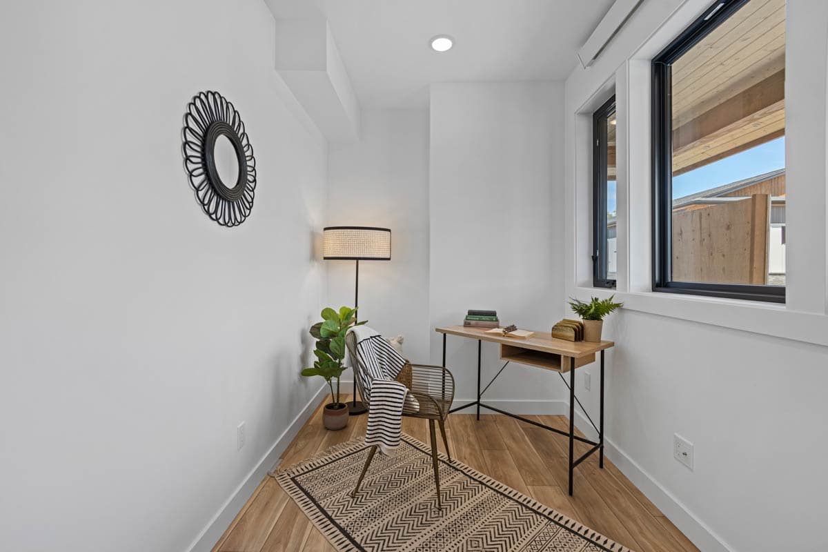 Compact home office with a writing desk, chair, floor lamp, patterned rug, and large windows.