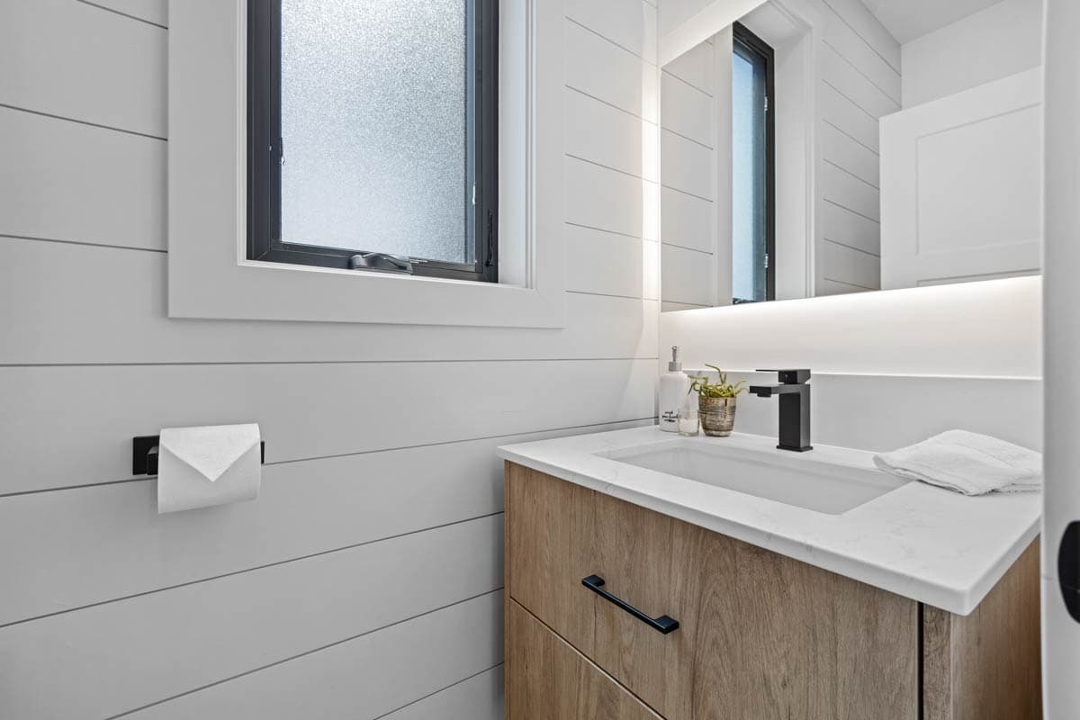 Bathroom with shiplap walls, single sink vanity with wood grain cabinets, black faucet, and frosted window.