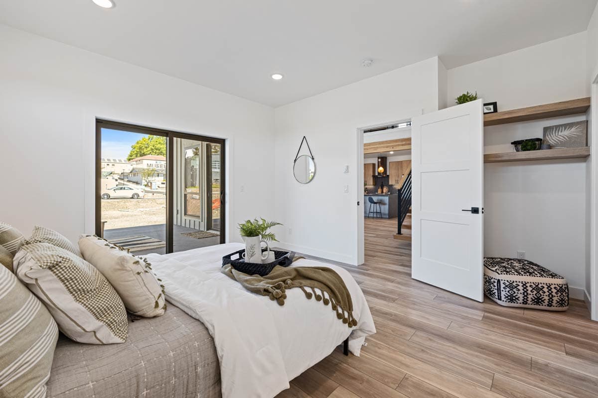 Bedroom with sliding glass doors, view of kitchen and open closet with shelving.