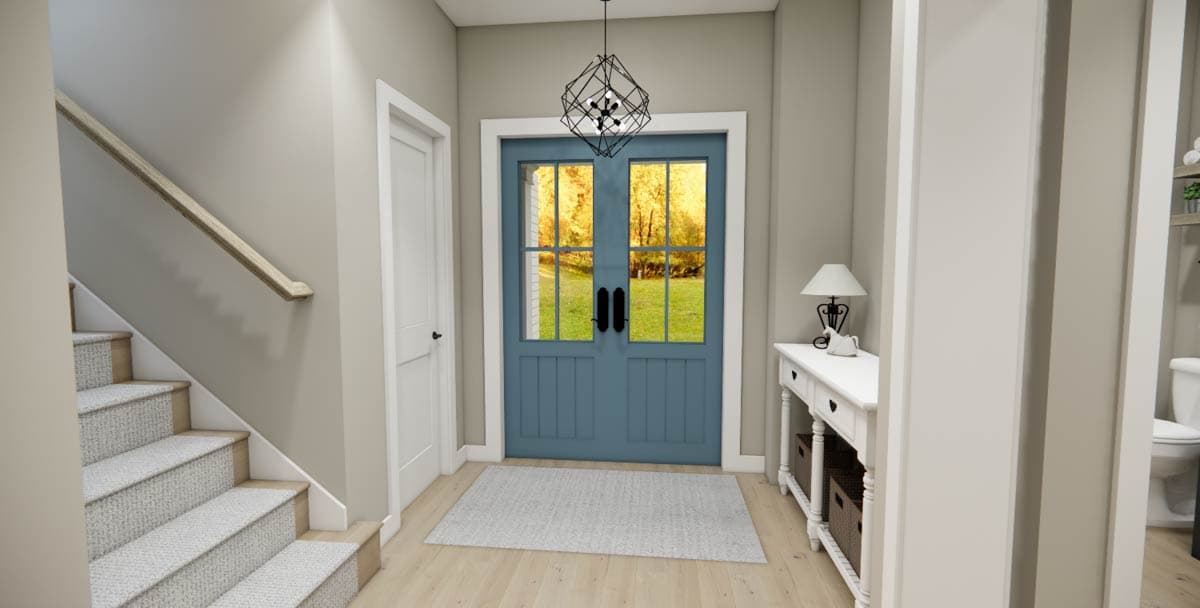 Interior view of entry hall with staircase, blue double doors with windows, and console table. Modern light fixture.