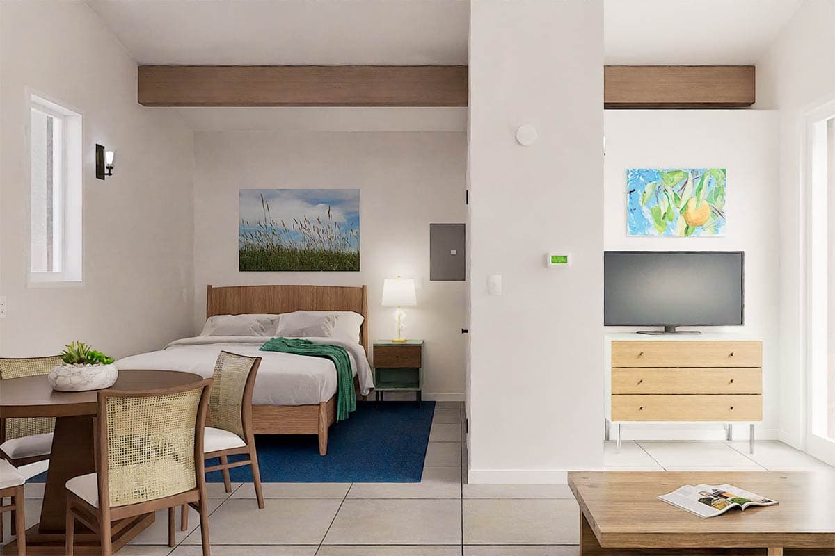 Bright, modern interior with a bedroom and living space. Includes a bed with art, a dining area, and a television with a wood dresser.