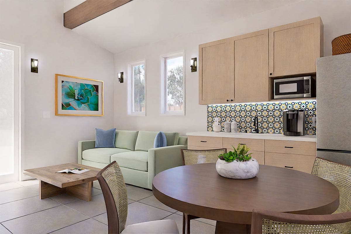 Bright, modern living space combines a small kitchen with a seating area. Includes a sofa, round table, and a colorful tile backsplash.