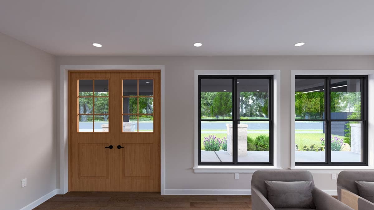 Interior view of a room with double wooden doors with glass panes and two large black-framed windows overlooking a yard.