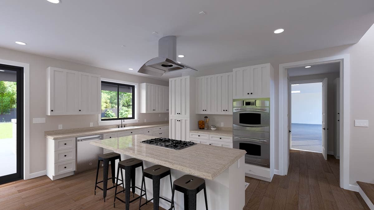 Modern kitchen with island cooktop, double ovens, white cabinetry, and granite countertops. Open doorway reveals adjacent room.