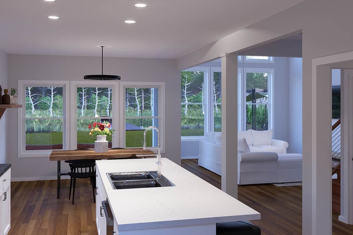 Open-concept kitchen and living area with island, dining table, and large windows overlooking a wooded area.