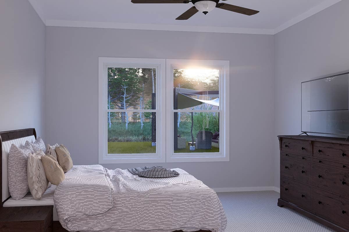 Bedroom interior with bed, dresser, ceiling fan, and double window overlooking a backyard.