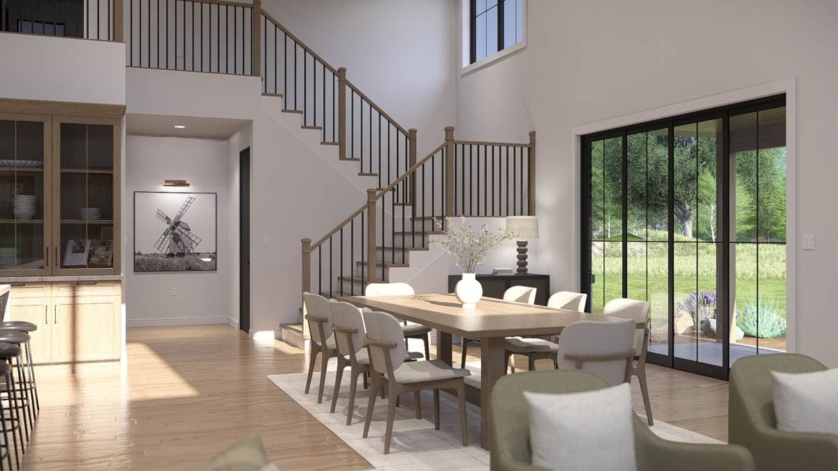 Dining room with a long table, chairs, and a grand staircase. Large sliding doors offer views of a grassy yard.