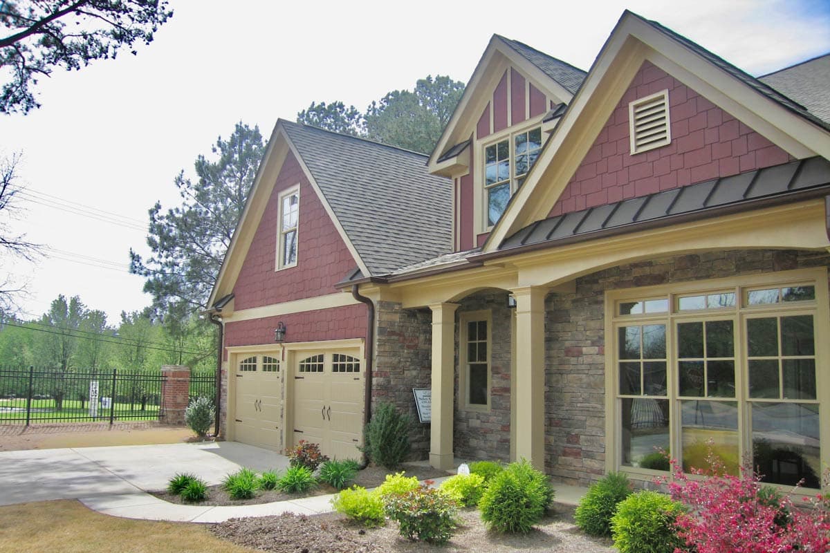 House plan exterior with stone and shingle siding, arched entry, and a side-facing two-car garage.