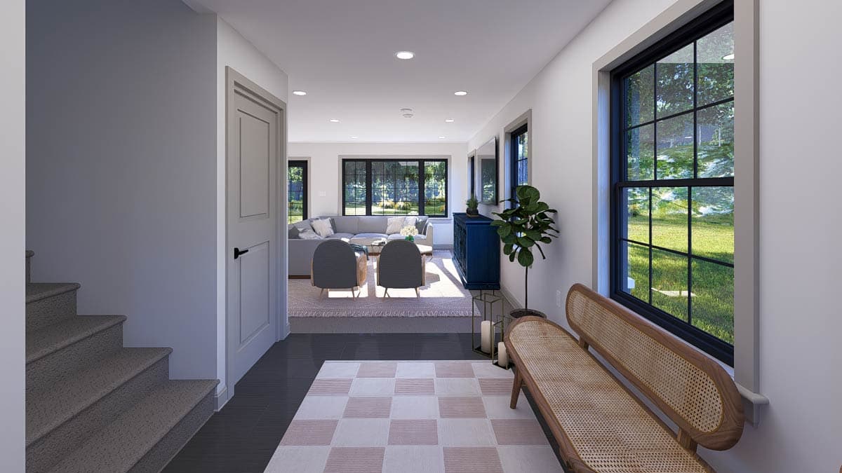 Interior view of a living room with a sectional sofa, large windows, and stairs leading to another level.