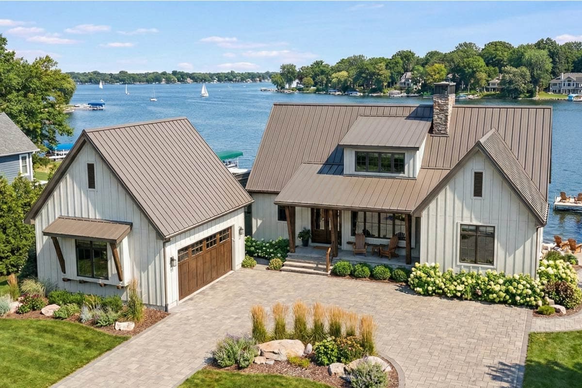 Modern farmhouse exterior with metal roof, gabled dormer, stone chimney, and attached garage with wood door.