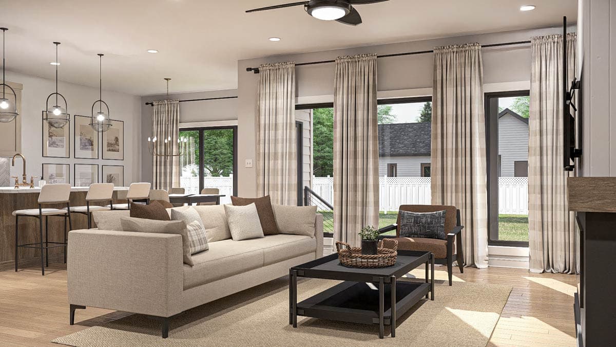 Open-concept living space with a sofa, coffee table, kitchen island with bar stools, and dining area, featuring large windows and a ceiling fan.