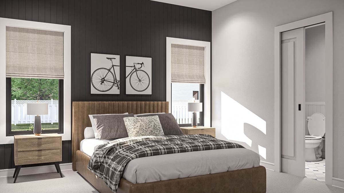 Bedroom with a queen bed, dark paneled wall, two windows with roman shades, and a sliding door revealing a toilet.