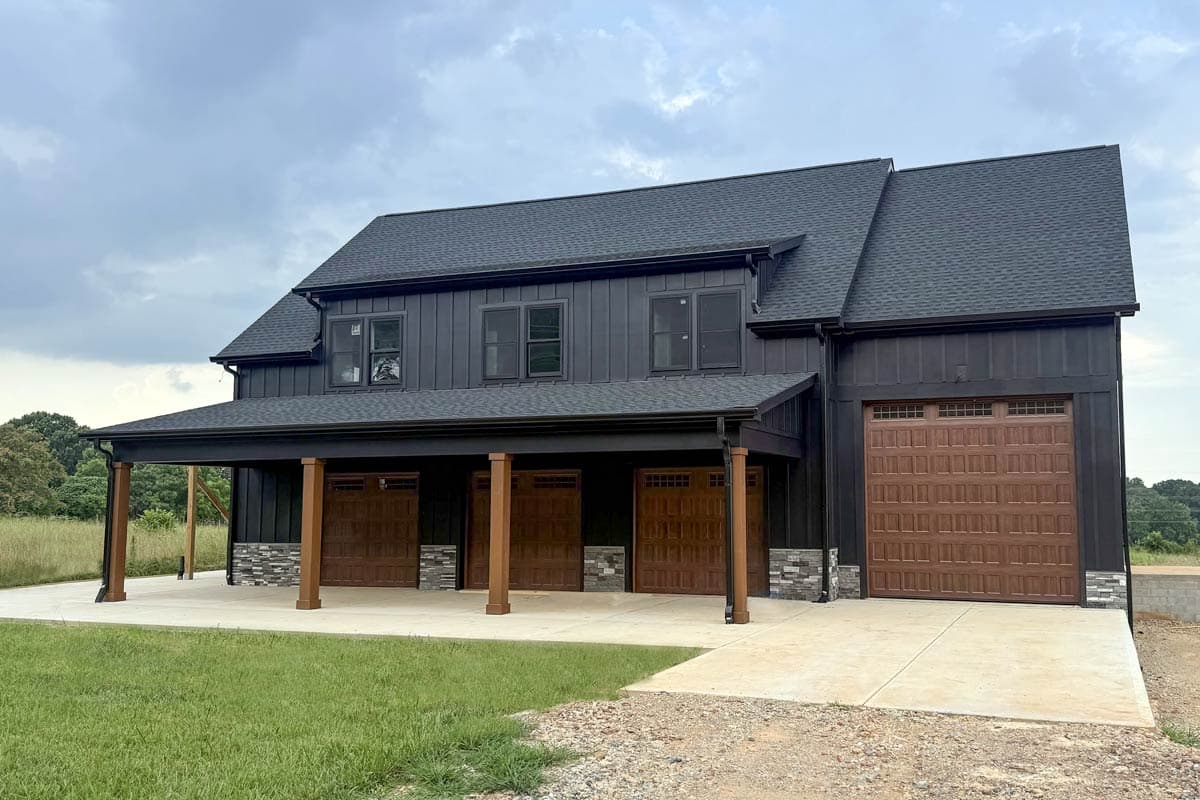Modern Farmhouse house plan exterior with dark vertical siding, a covered porch supported by wood columns, and four garage bays with brown doors.
