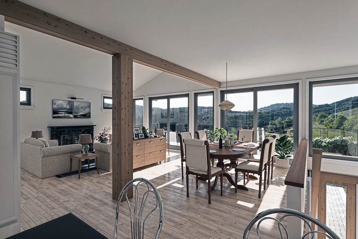 Open-concept living and dining area with exposed wood beams, fireplace, and large windows overlooking a hillside.