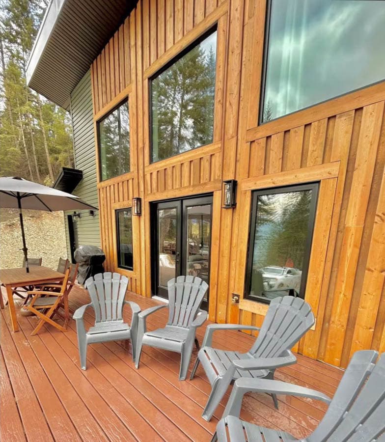 House plan exterior with wood siding, large windows, glass doors, and a deck with Adirondack chairs.