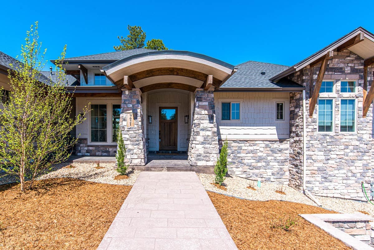 House plan exterior featuring stone and shingle siding, a prominent arched entryway with timber supports, and multiple gables.