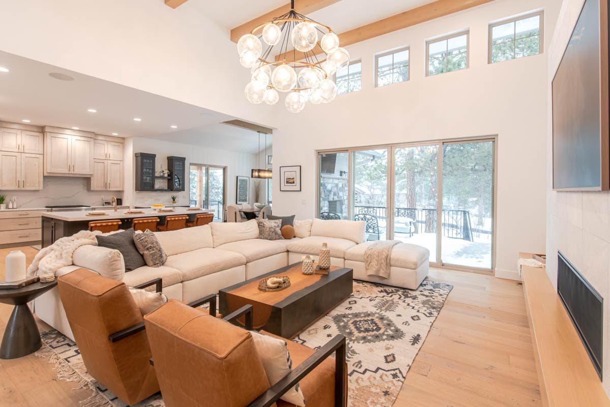 Modern open-concept living space with vaulted ceilings, exposed beams, large windows, and a sectional sofa.