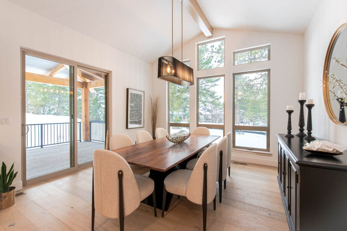 Dining room with vaulted ceiling, large windows, and access to a deck. Includes a wooden table and chairs, and a sideboard.