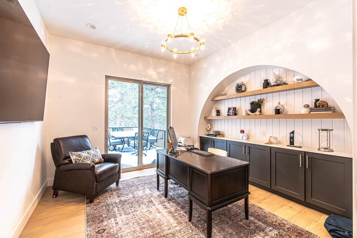 Office interior featuring a dark wood desk, leather armchair, built-in shelving with arched niche, and sliding glass doors to a balcony.