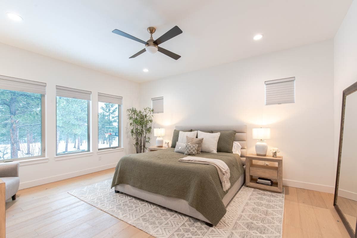 Bedroom with king bed, large windows, ceiling fan, and wooden floors.