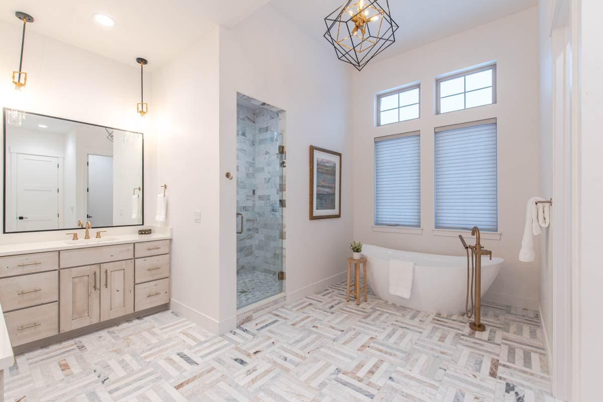 Modern bathroom with freestanding tub, glass-enclosed marble shower, double vanity, and geometric pendant light.
