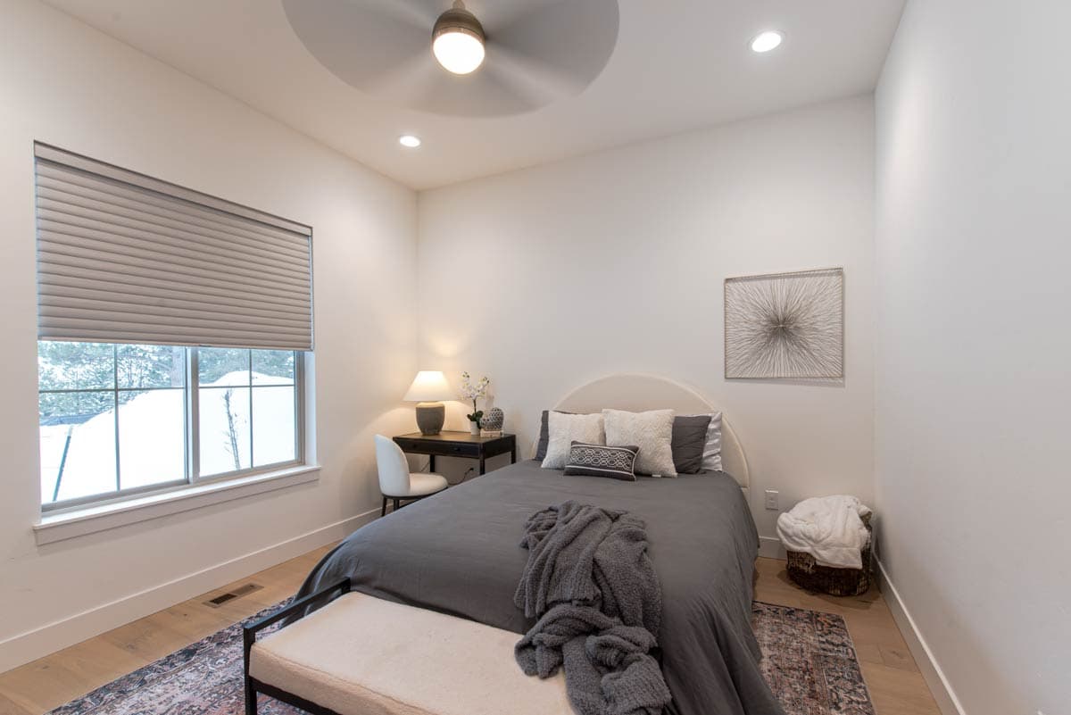 Bedroom with bed, desk, window with blinds, ceiling fan, and wall art.