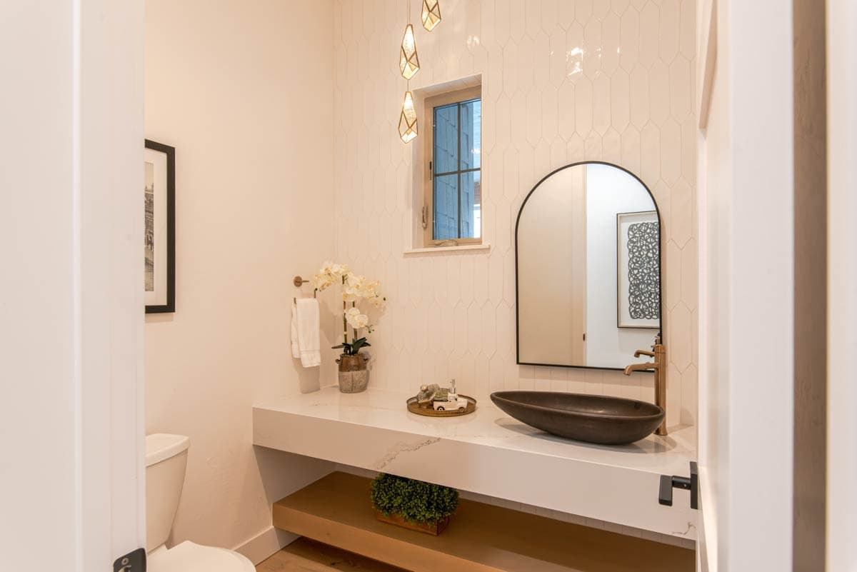 Powder room with tiled walls, floating vanity, vessel sink, arched mirror, and modern pendant lights.