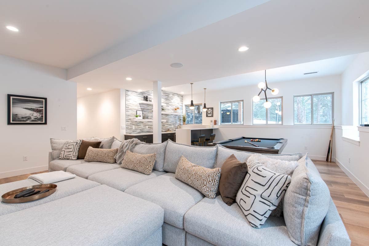 Modern basement recreation room with sectional sofa, pool table, and wet bar. Open layout with bar seating and wall accent.