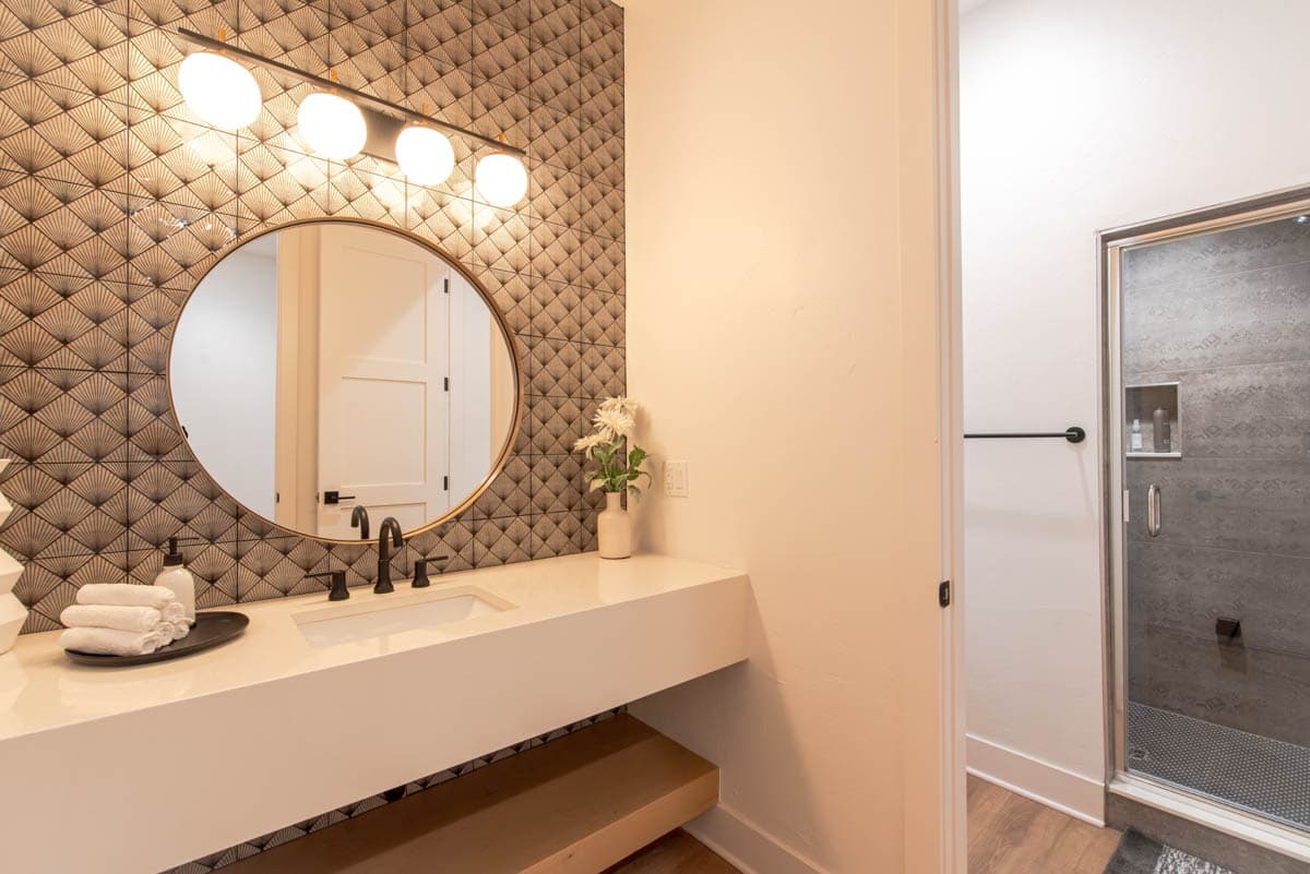 Bathroom vanity with a white countertop, oval mirror, geometric tile backsplash, and shower stall.