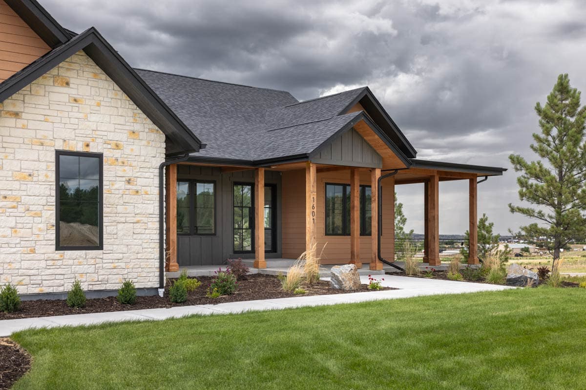 House plan exterior with stacked stone, vertical siding, exposed rafter tails, and covered porch with timber posts.