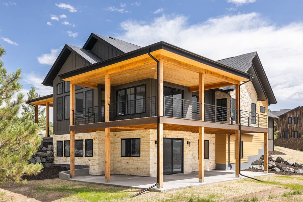 Modern house plan exterior featuring stone and wood siding, multiple gables, and a large covered deck with wood soffits.