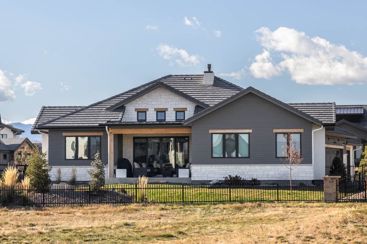 House plan exterior with a mix of stone and siding, covered patio with large windows, and multiple gables.