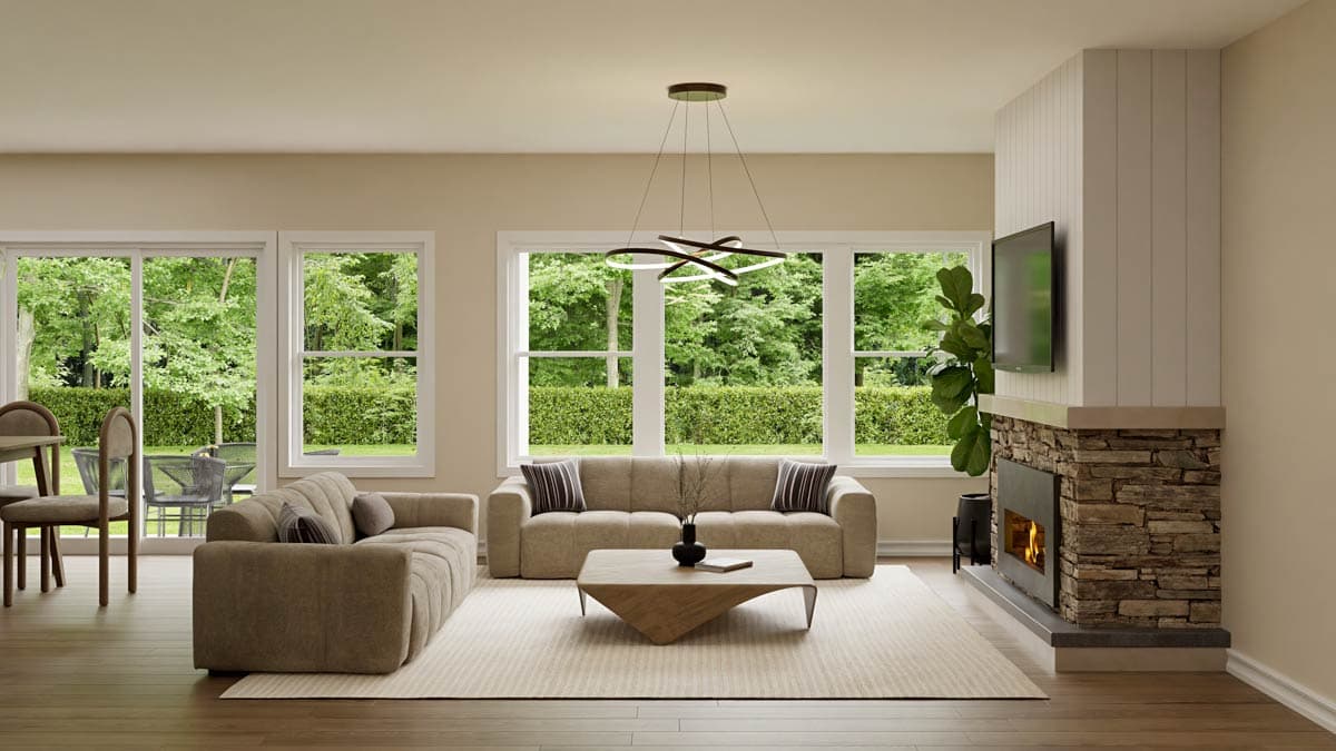 A modern living room with a stone fireplace, beige sofas, and large windows overlooking a lush green garden. A contemporary light fixture hangs above.