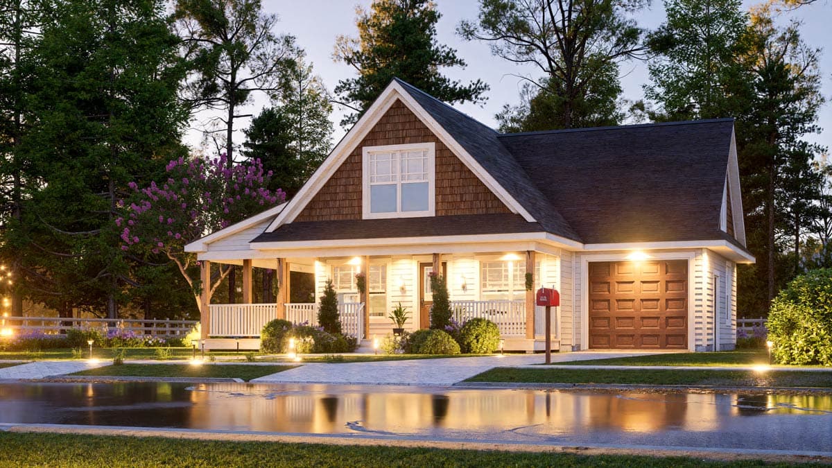 A charming white house with a porch and brown shingles is lit up, reflecting in a wet street on a cloudy day.