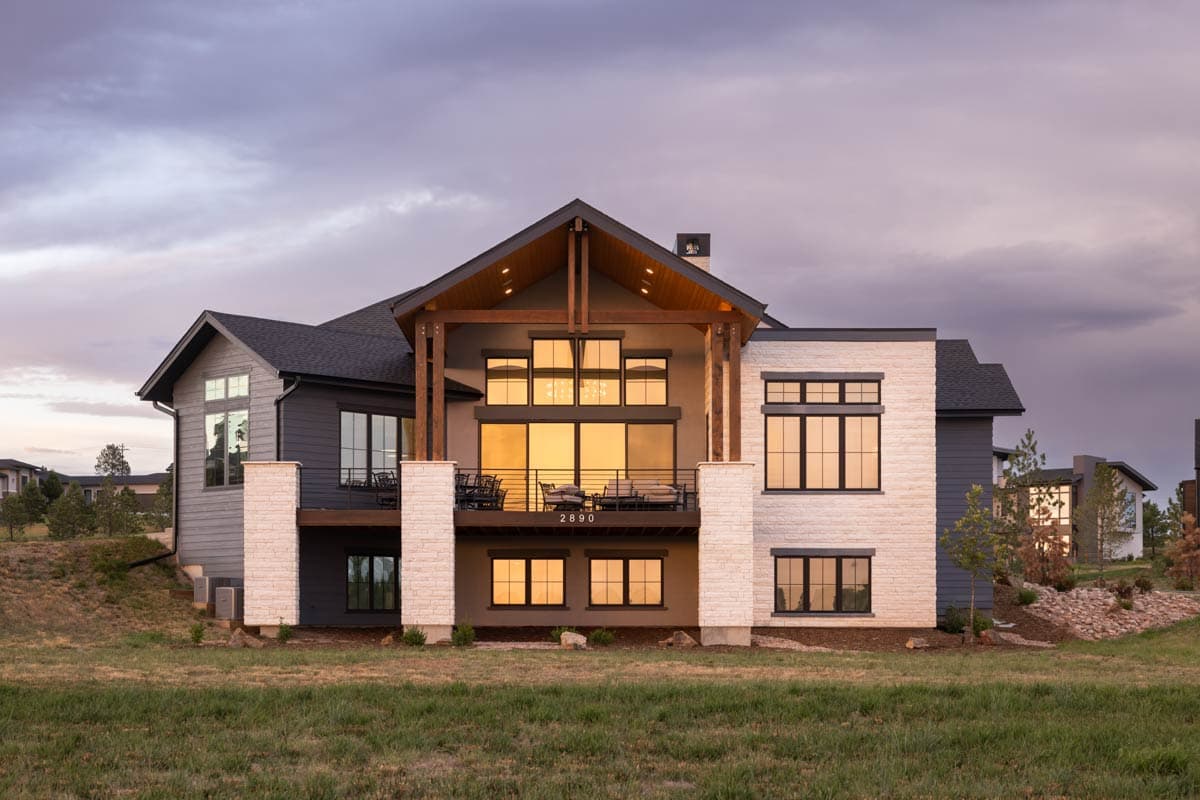 Modern house plan exterior with stone and dark siding, a covered deck with large windows, and a prominent gable roof.