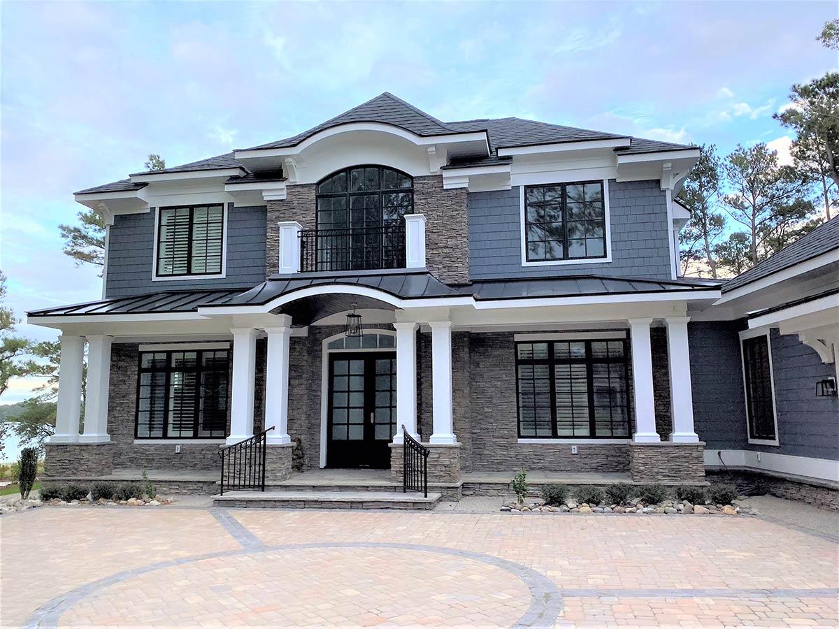House plan exterior: Two-story home with stone and shingle siding, prominent columns, and a curved balcony.