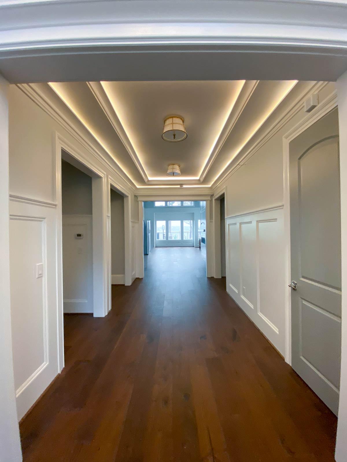 Hallway with coffered ceiling, inset lighting, wood floor, and multiple doors leading to rooms and an open living area.