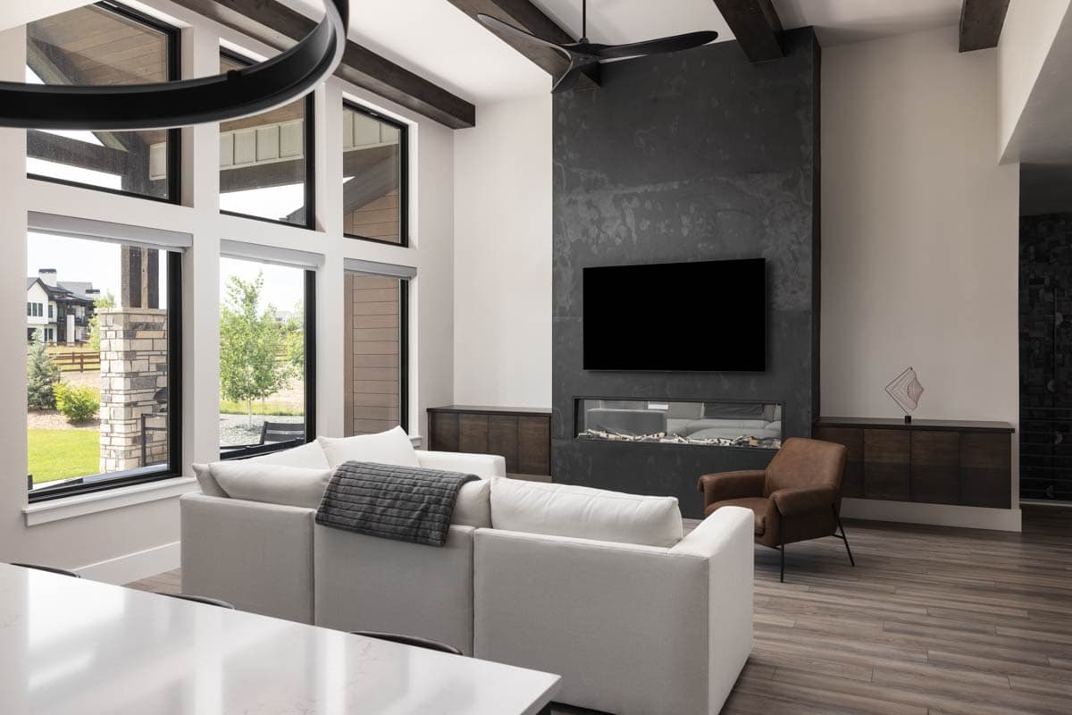 Interior rendering of a living room with a floor-to-ceiling fireplace, large windows, exposed beams, and a sectional sofa.