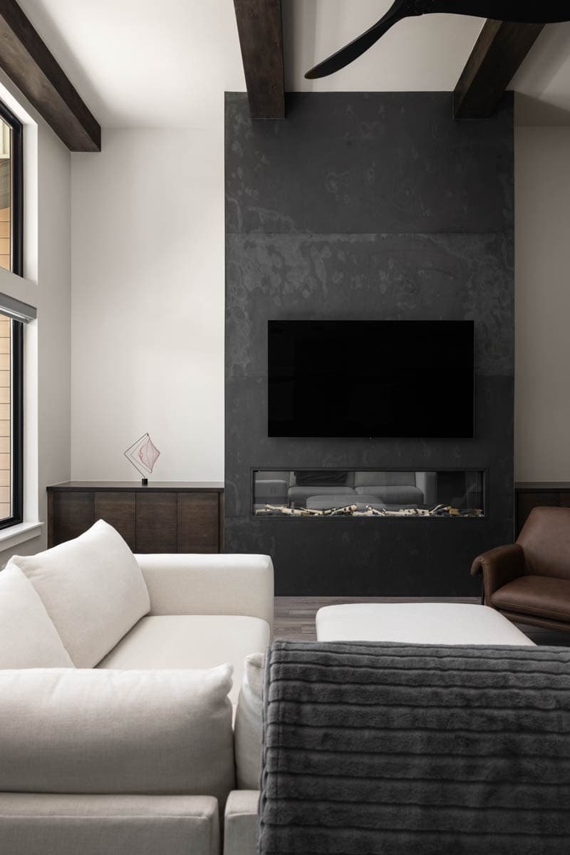Living room with a floor-to-ceiling stone fireplace, mounted television, and exposed wooden beams.